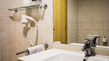A bathroom with a white sink, a glass shelf with toiletries, a hairdryer, and a toilet visible in the reflection.