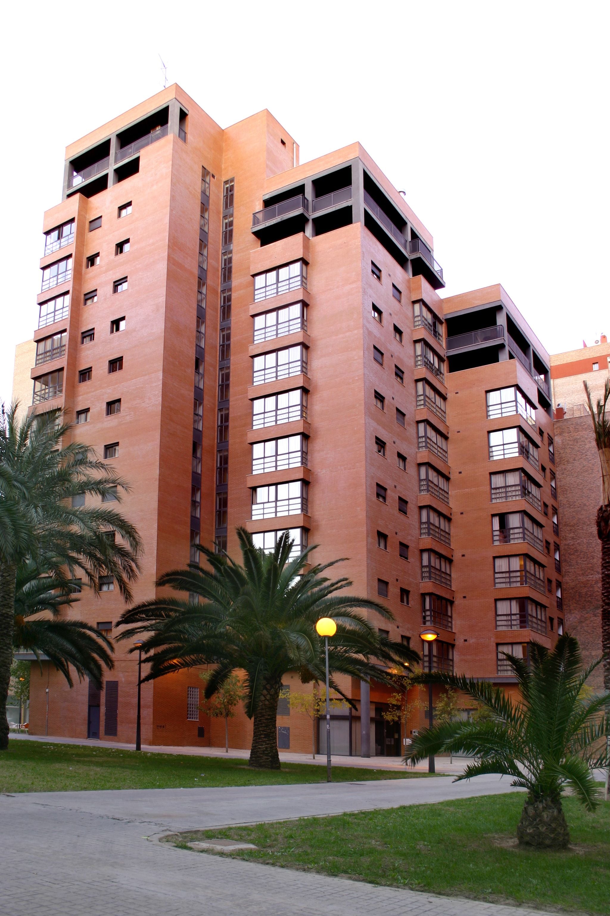 A multi-story building with balconies, a paved walkway, and palm trees.