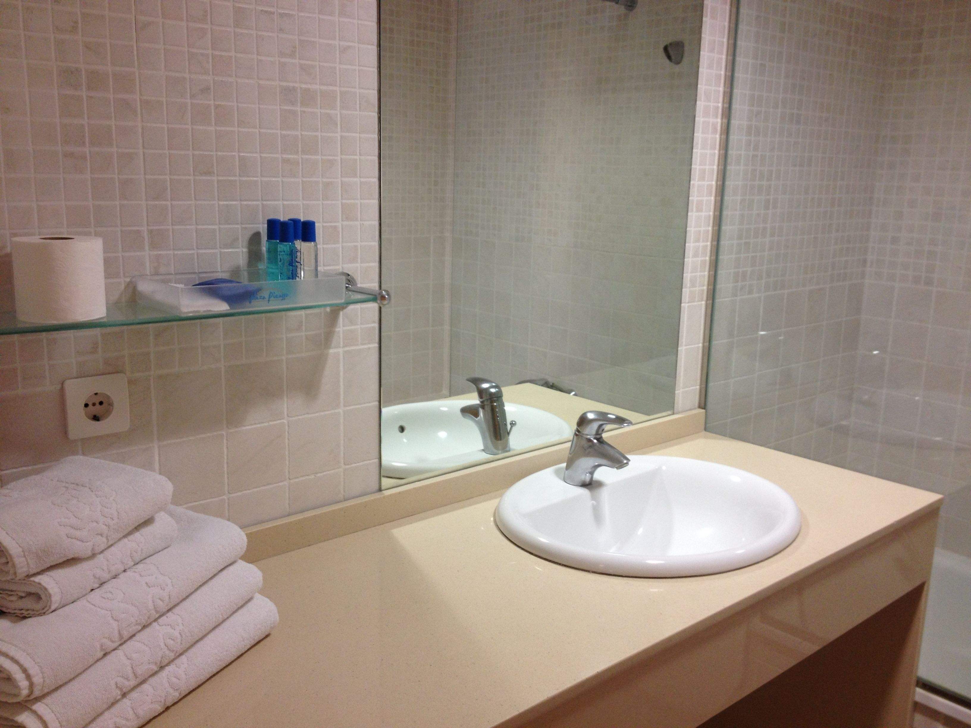 A bathroom with a white sink, a glass shelf with toiletries, and a stack of white towels.