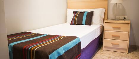 A neatly made bed with a striped blanket, a bedside lamp, and a wooden nightstand with drawers.
