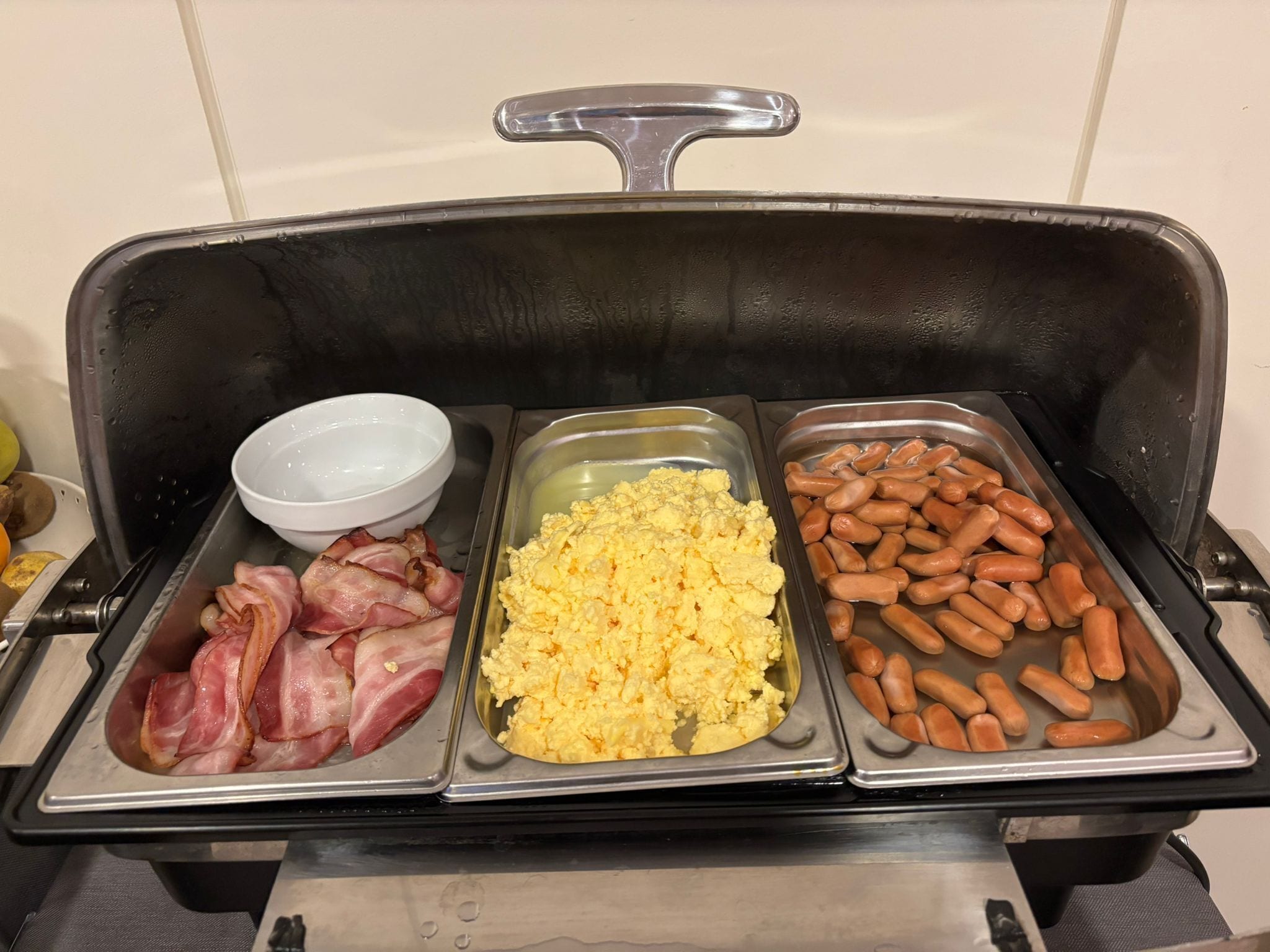 A buffet with bacon, scrambled eggs, and sausages.