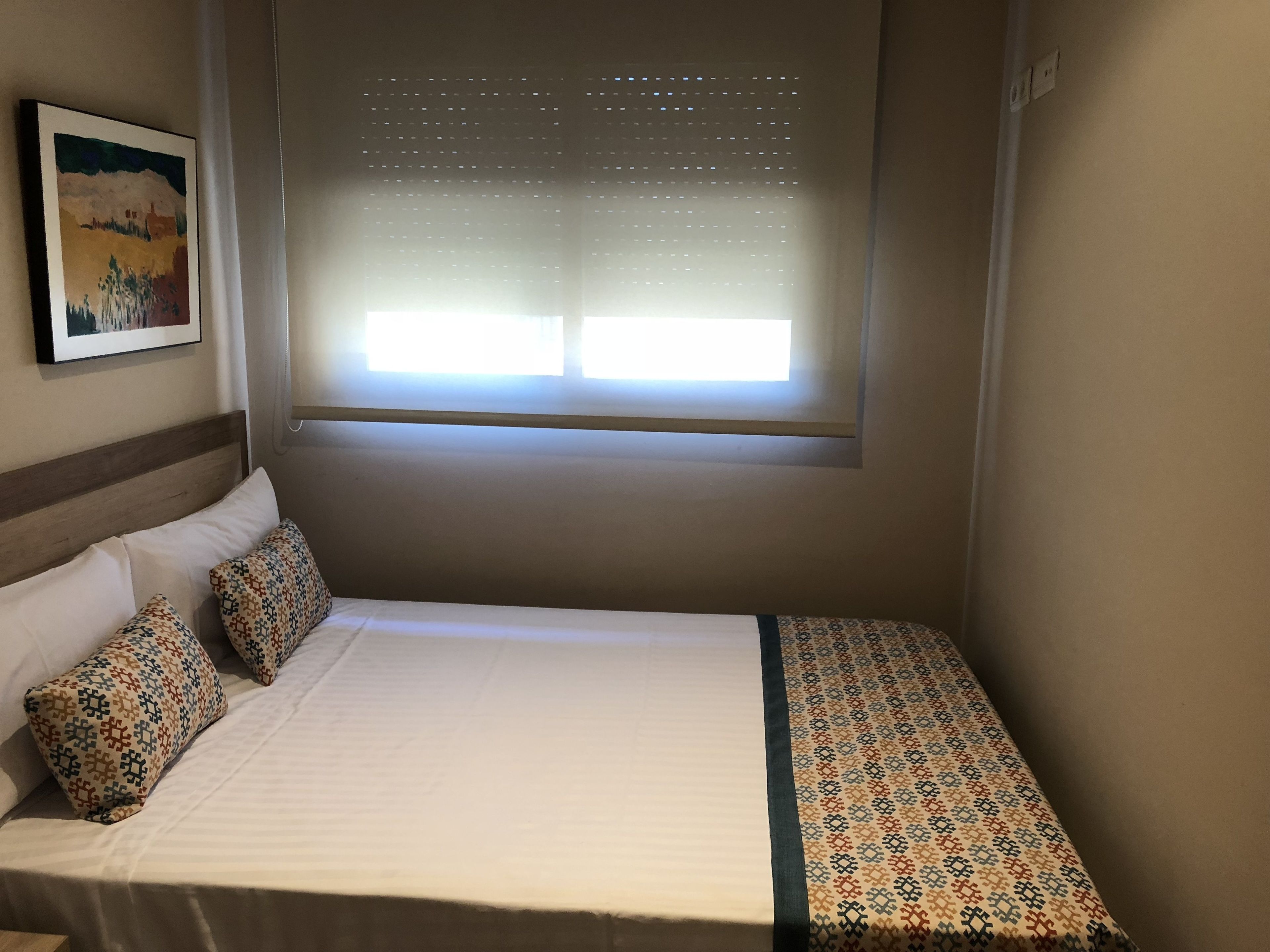 Un lit simple avec des coussins à motifs, une couvre-lit unie et une fenêtre avec des stores.