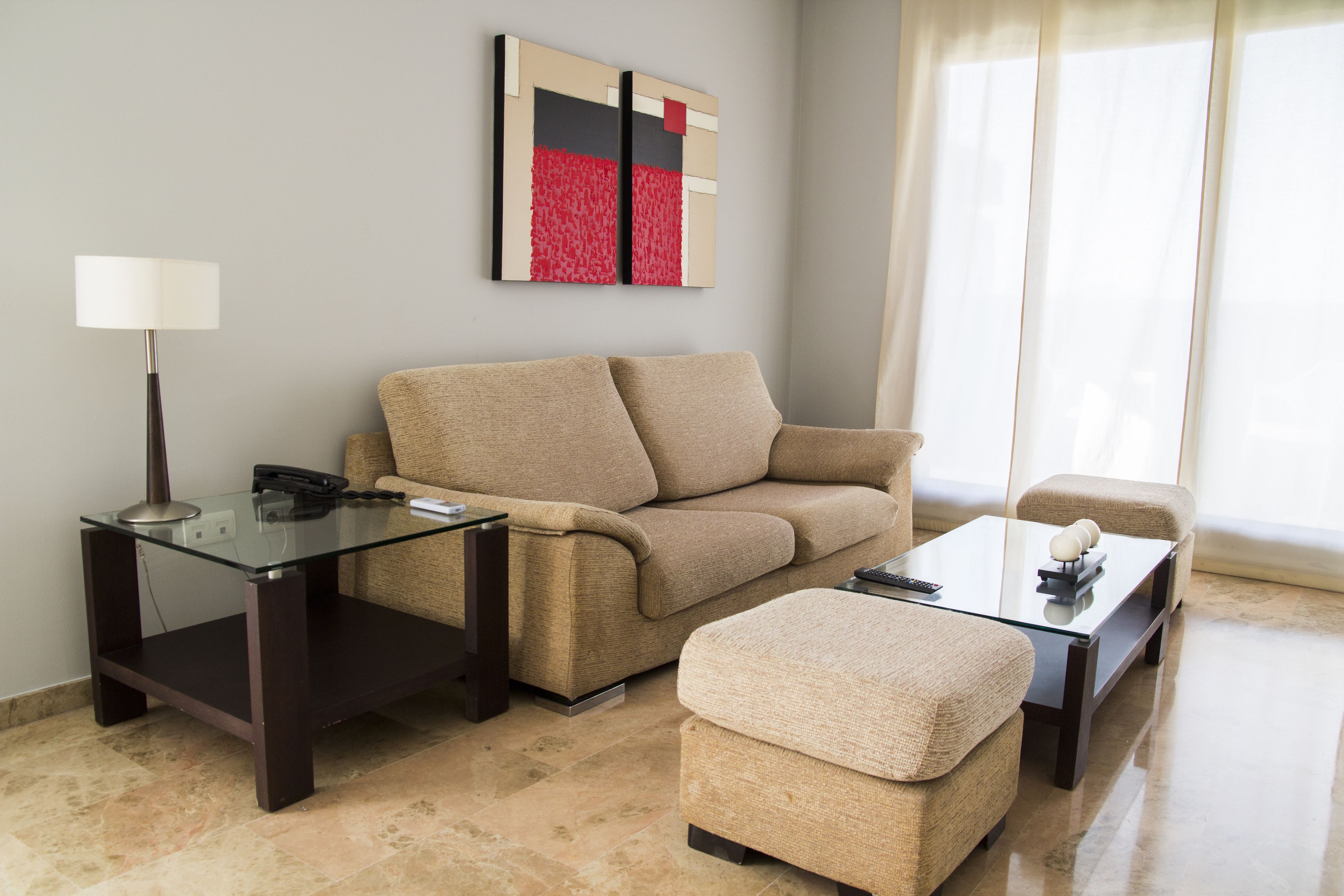 A modern living room with a beige sofa, a glass coffee table, and a glass side table with a lamp.