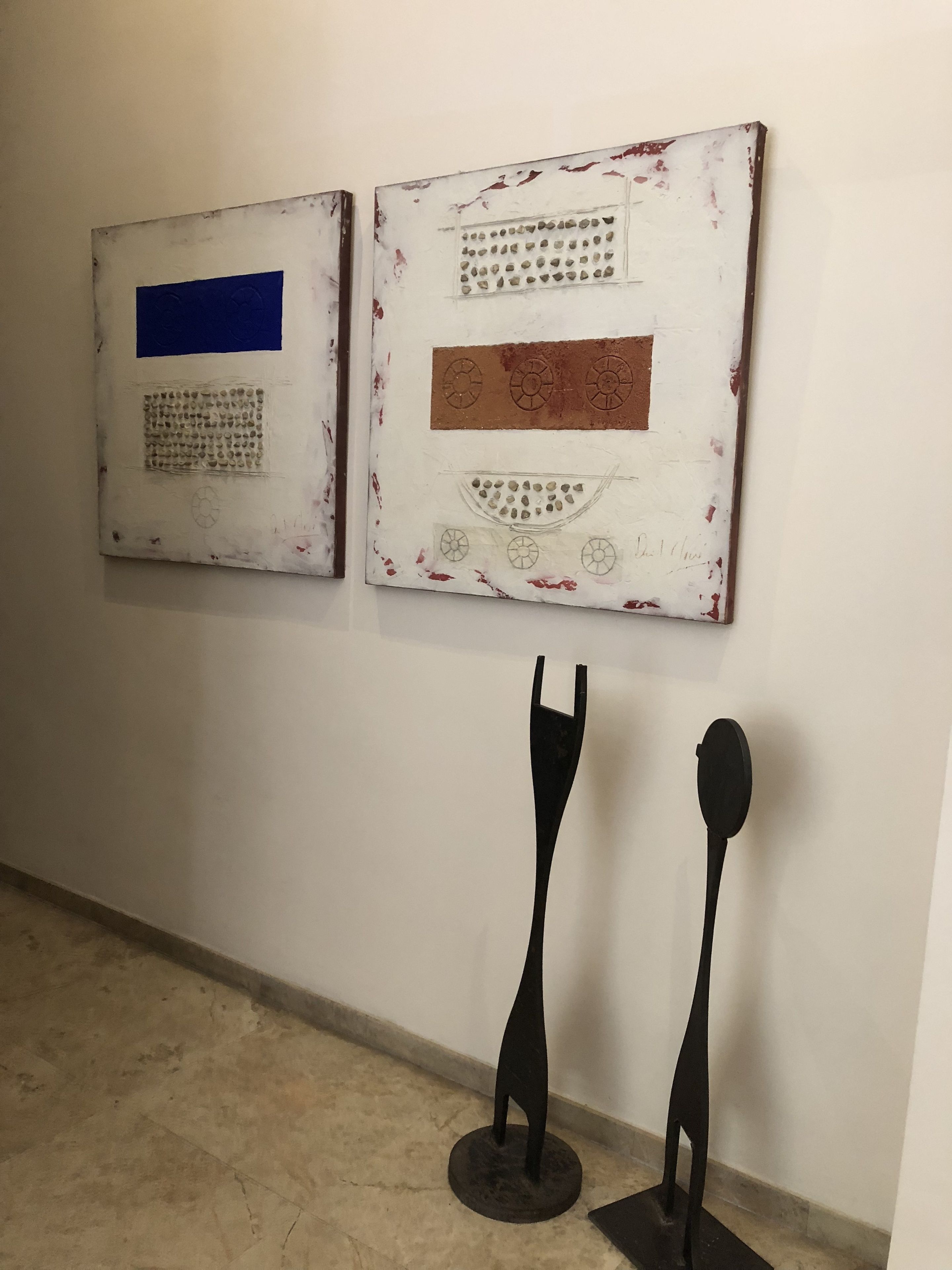Dos pinturas abstractas en una pared, un par de esculturas negras en el suelo.
