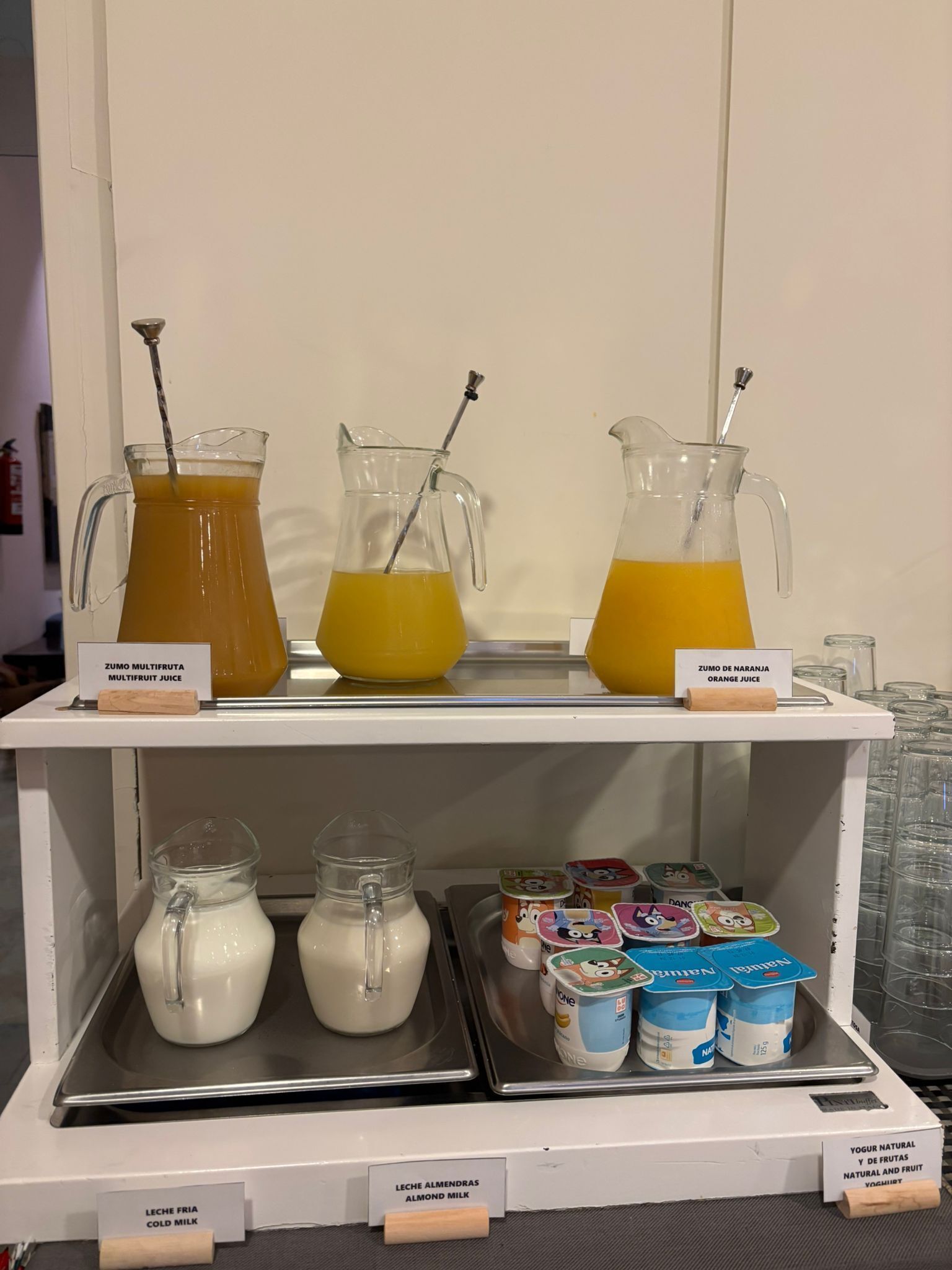 A beverage station with two pitchers of juice and two pitchers of milk, along with yogurt containers.
