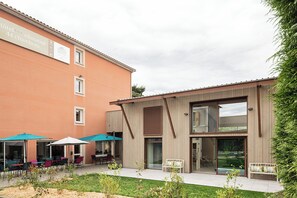 A hotel with a modern exterior, outdoor seating area, and a visible entrance. - Deltour Hotel Puy en Velay (Brives-Charensac)