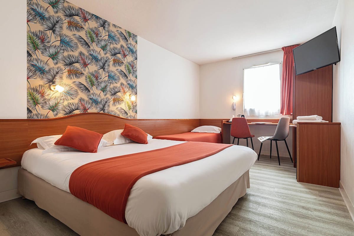 A hotel room with two beds, a desk, a chair, a TV, and a wall with a leaf pattern.