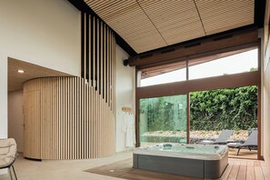 Un moderno espacio de spa con un jacuzzi, sillones reclinables y un ventanal grande con vistas a un jardín.