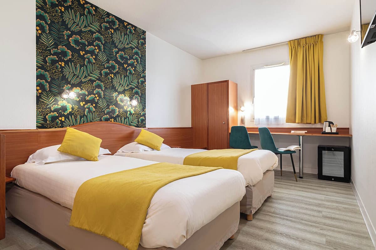 A hotel room with two beds, a desk, a chair, and a small refrigerator.