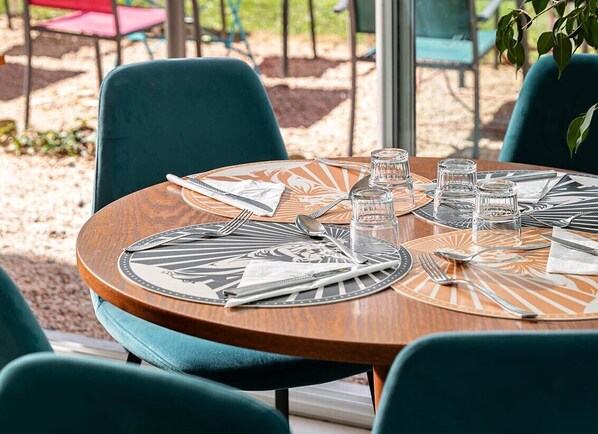A round table with a wooden top and a black and white patterned placemat, surrounded by teal chairs.