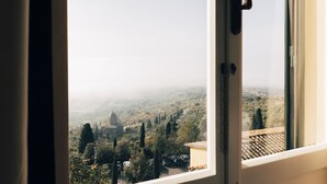 A window view of a town with buildings, trees, and parked cars. - Hotel San Luca (Cortona)