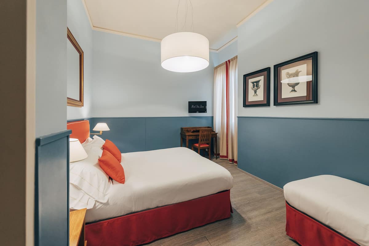 A hotel room with a bed, bedside table, lamp, and two framed pictures on the wall.