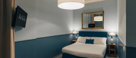 Una habitación de hotel con cama, mesitas de noche, un espejo y televisor.