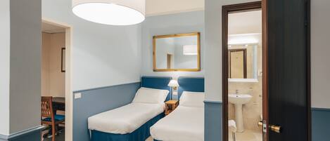 A room with two single beds, a desk, a chair, a mirror, and a door leading to a bathroom.