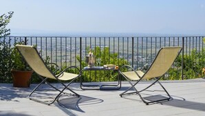 A balcony with two lounge chairs, a small table with a drink, and a scenic view. - Hotel San Luca (Cortona)