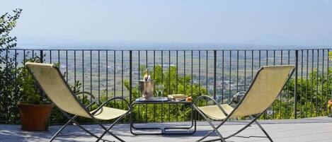 Un balcon avec deux fauteuils, une petite table sur laquelle se trouve une boisson, et une vue panoramique.