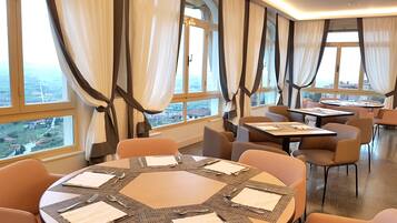A restaurant with round tables, chairs, and large windows with curtains.
