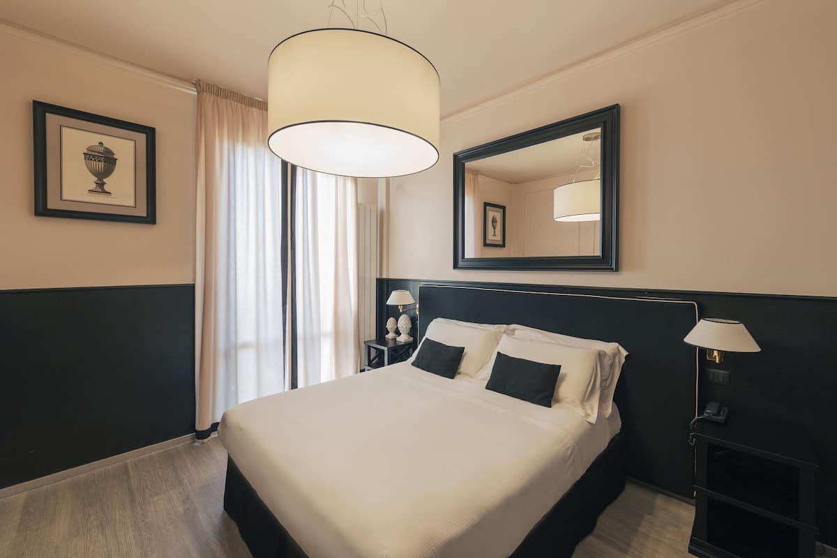 A hotel room with a large bed, a bedside table with a lamp, a mirror, and a framed picture on the wall.
