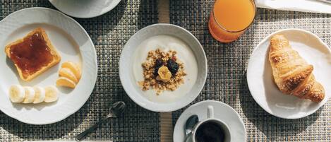 A breakfast setting with toast, fruit, yogurt, croissant, coffee, and orange juice on a woven tablecloth.