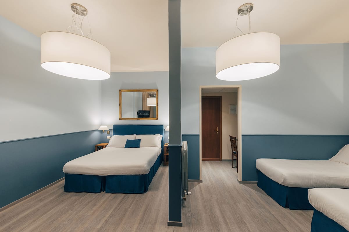 A hotel room with two beds, a large mirror, a radiator, and a wooden floor.