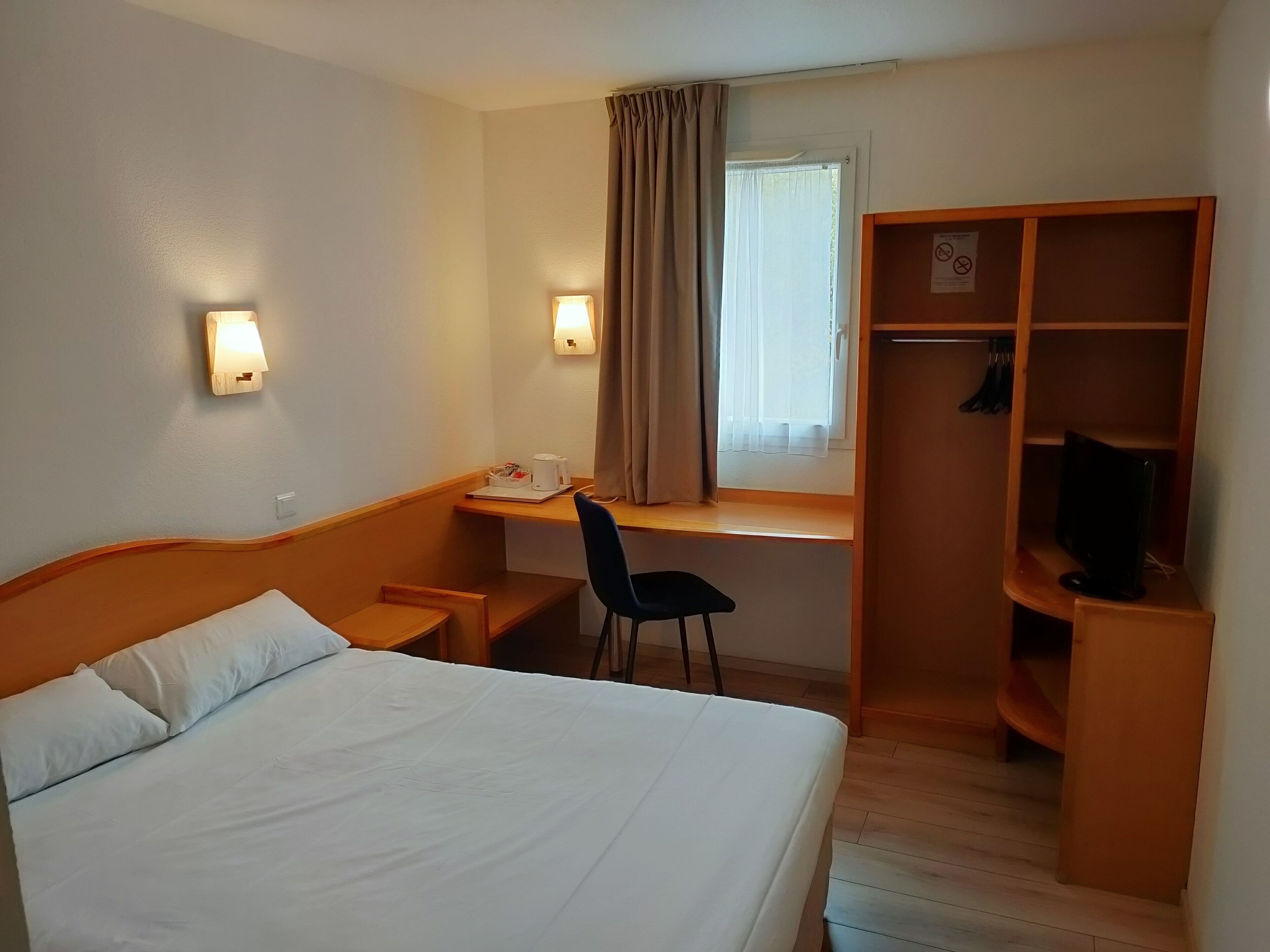 A hotel room with a bed, desk, chair, and a wardrobe.