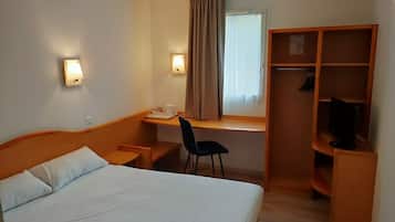 A hotel room with a bed, desk, chair, and a wardrobe.