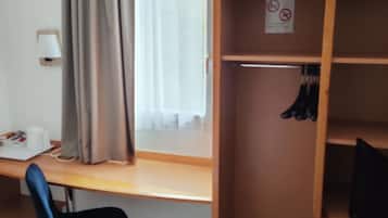 Una stanza con una scrivania in legno, una sedia, un armadio e una finestra con tende.