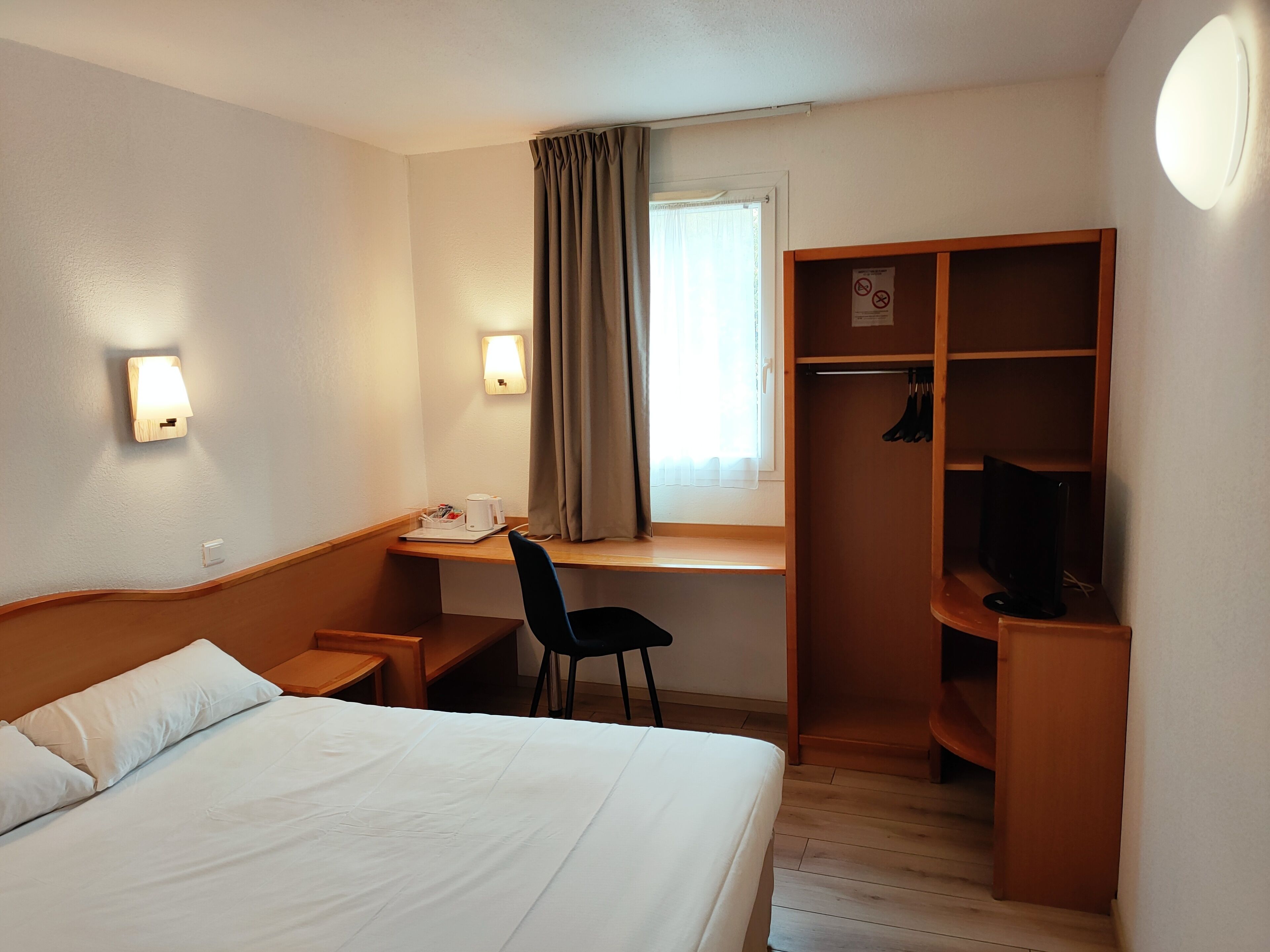 Una habitación de hotel con cama, escritorio, silla, televisor y armario.