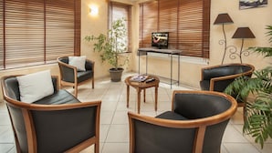 Une pièce comprenant quatre fauteuils en cuir noir avec des armatures en bois, une petite table en bois, une plante en pot et un téléviseur posé sur un meuble.