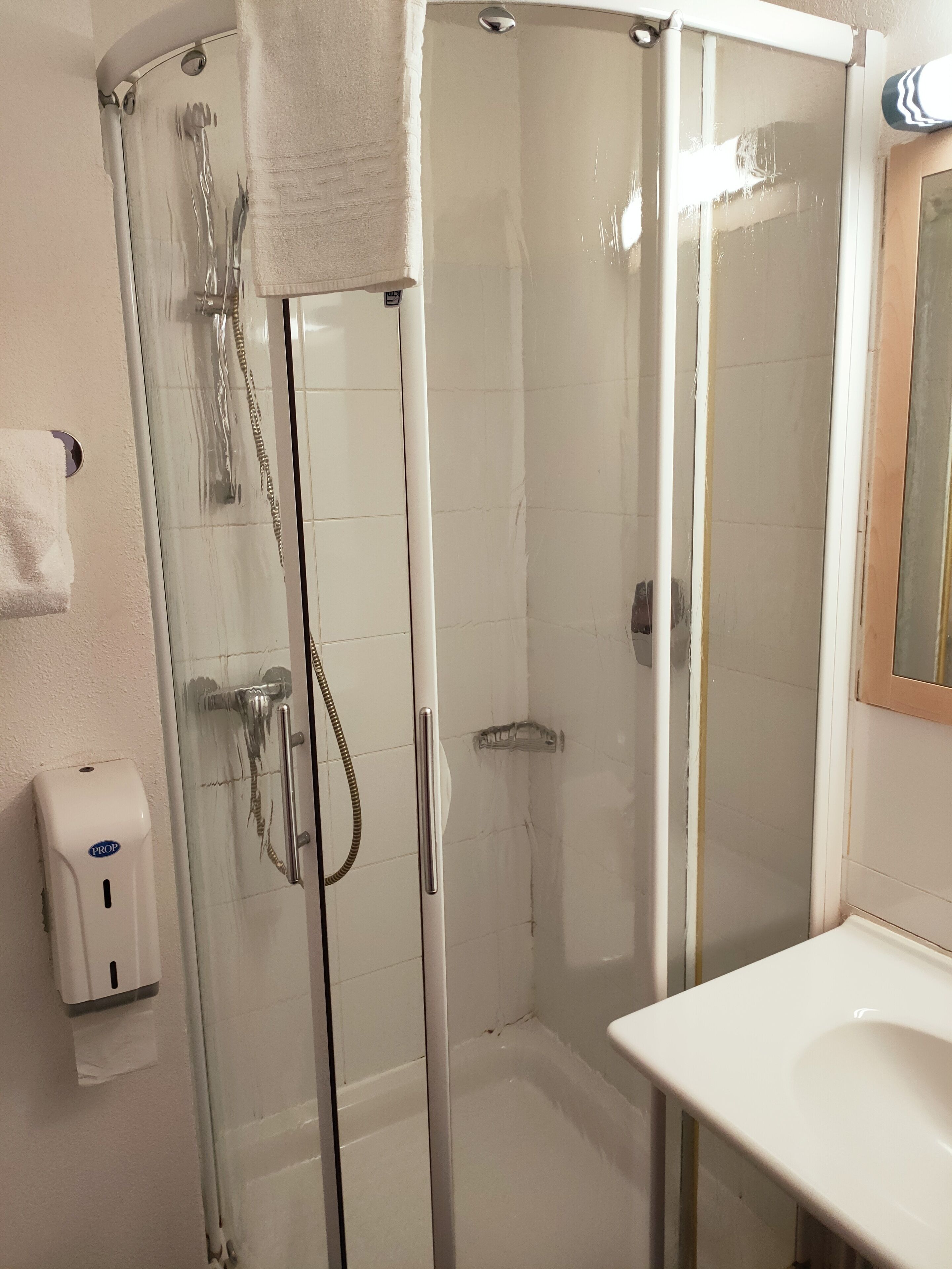 Un baño con ducha de vidrio, un lavamanos blanco y un secador de manos.
