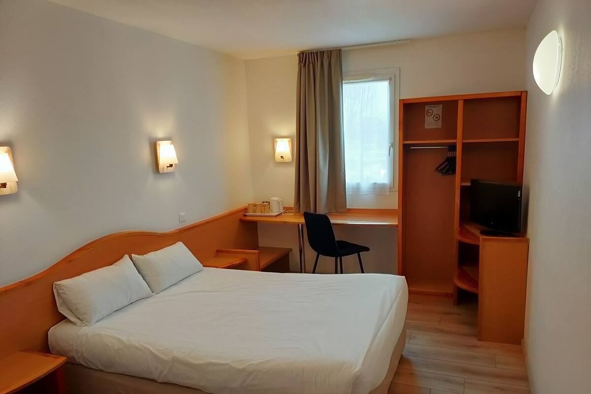 Une chambre d’hôtel avec un lit, un bureau, une chaise et un téléviseur.