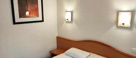 A hotel room with a neatly made bed, a framed picture on the wall, and two wall-mounted lights.