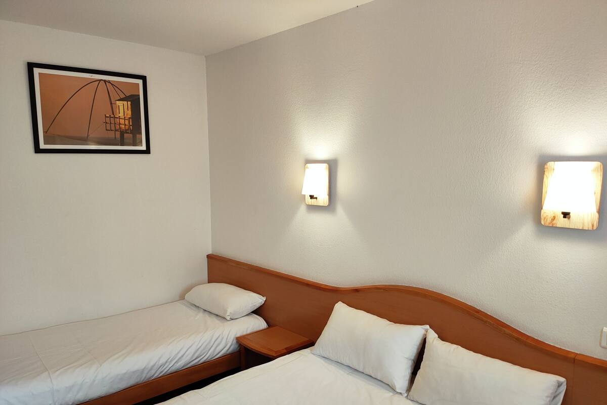 Une chambre d’hôtel avec deux lits simples, une tête de lit en bois et deux appliques murales.