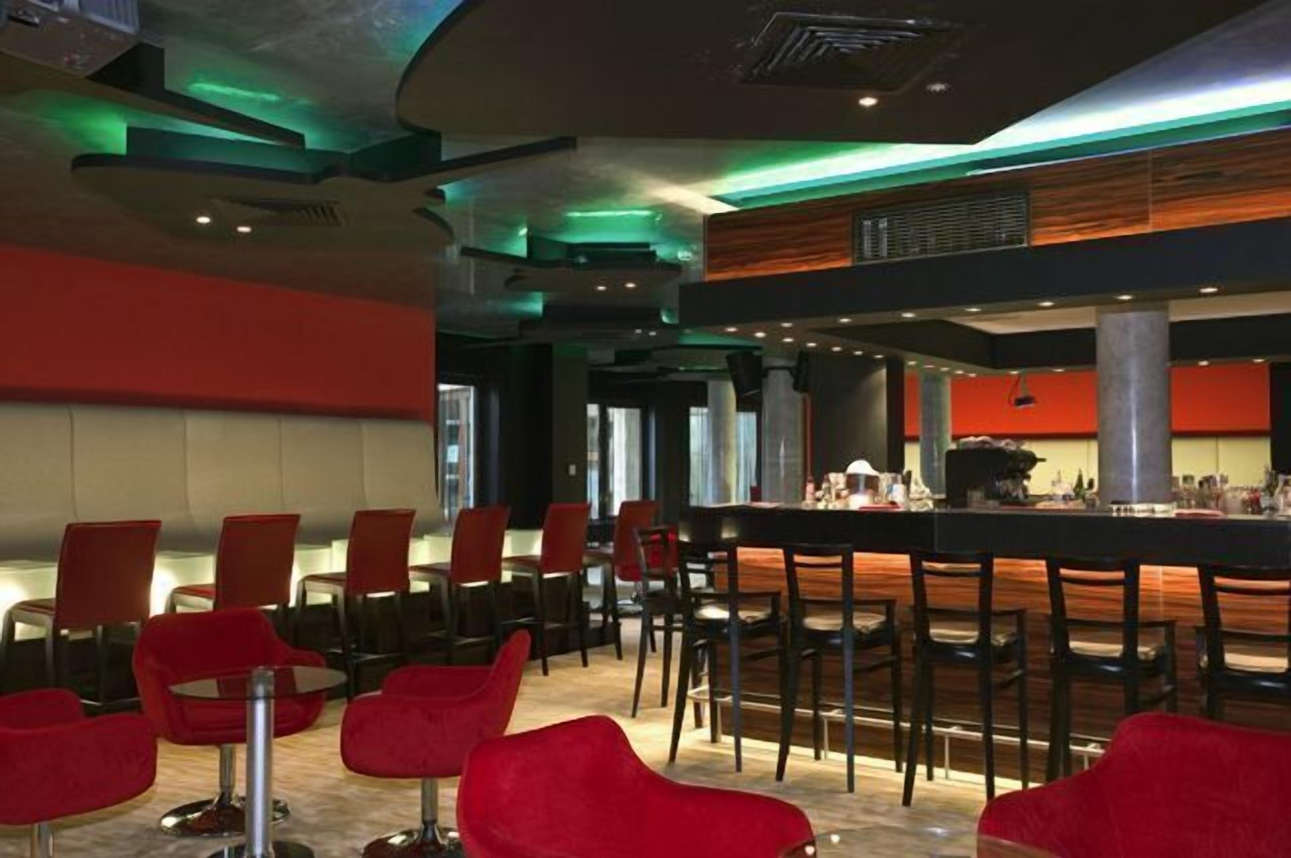Uma área de bar moderna com cadeiras vermelhas e um balcão comprido.