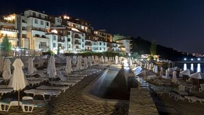 Un hotel sulla spiaggia con numerosi balconi, aree salotto all'aperto con ombrelloni e vista sul mare.