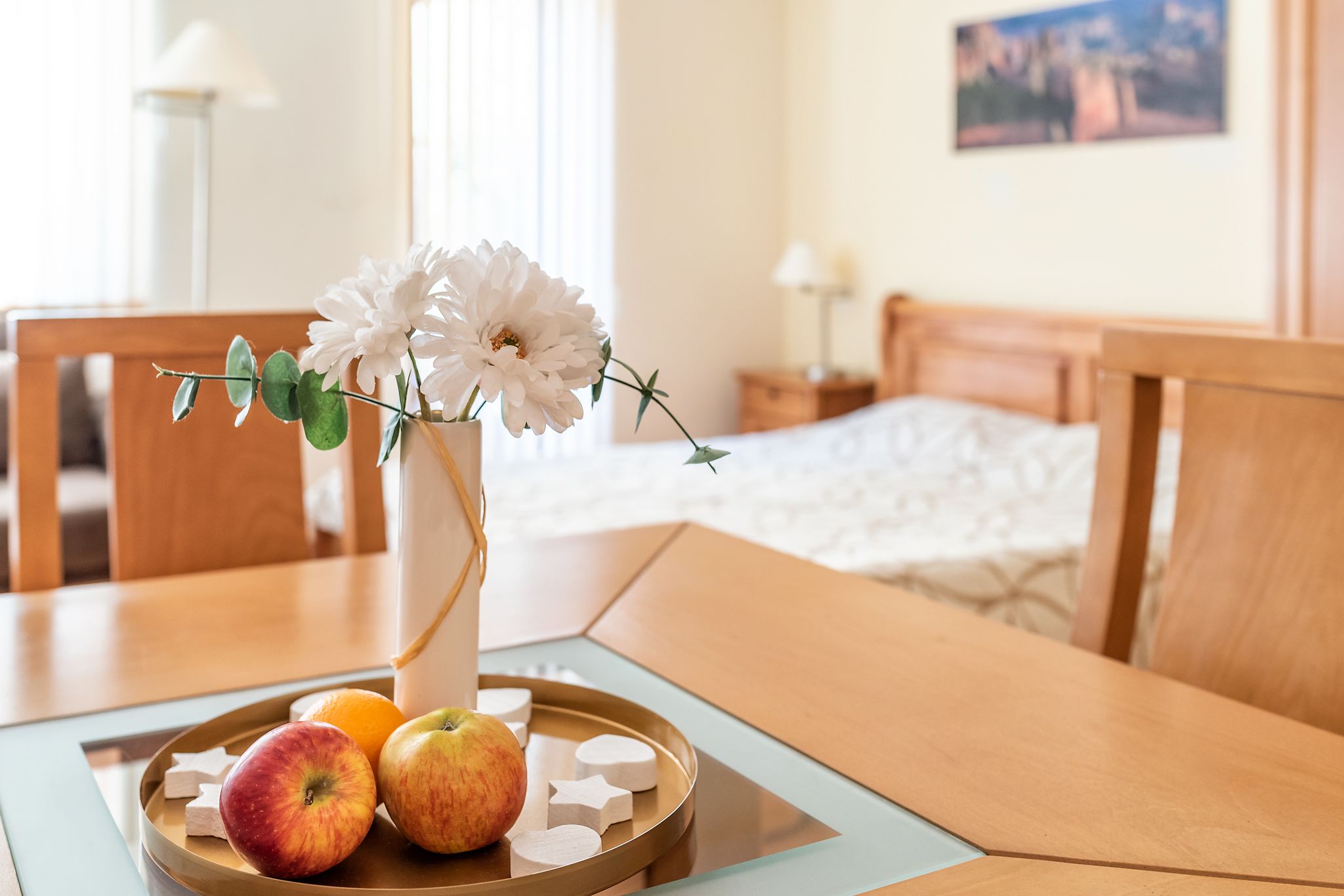 A dining table with a vase of flowers, apples, and oranges.