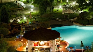 Una vista notturna di un resort con piscina, zona pranzo esterna coperta e un sentiero in giardino curato.
