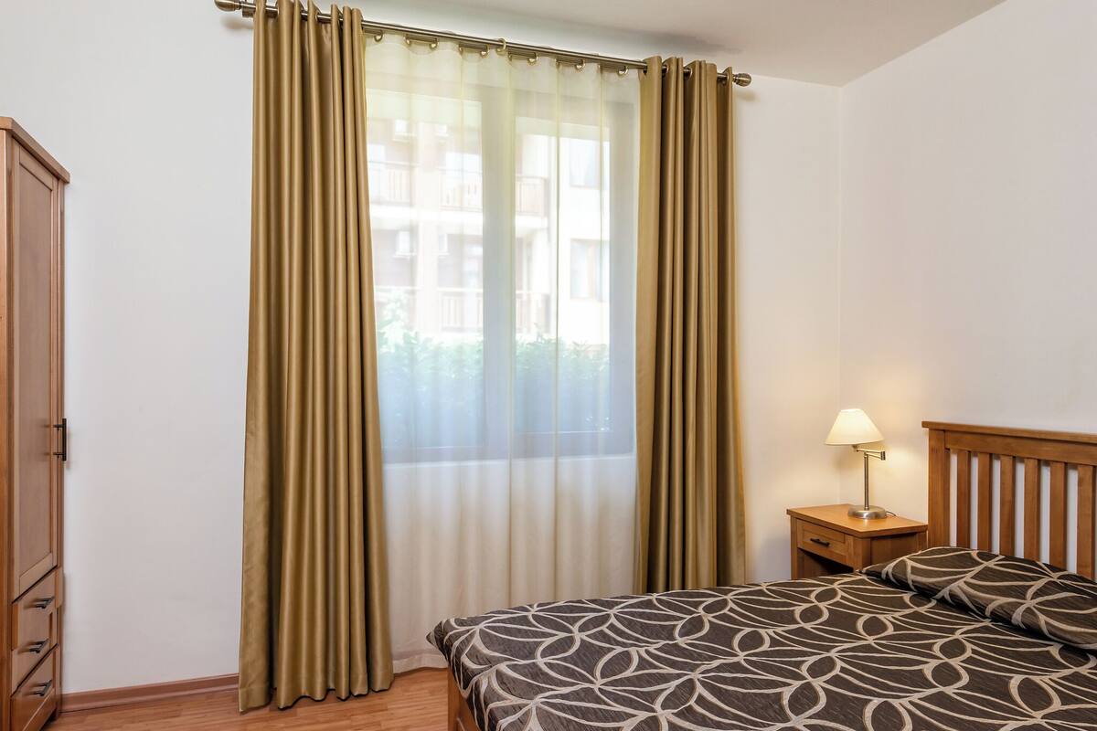 A bedroom with a bed, a nightstand with a lamp, and a window with curtains.