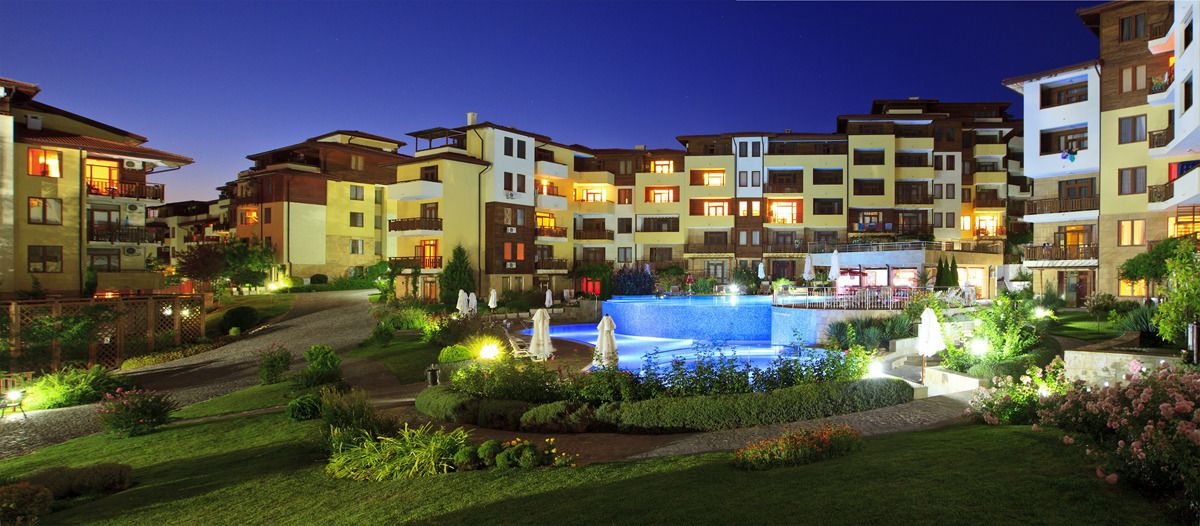 A hotel complex with multiple buildings, a swimming pool, and well-maintained gardens.
