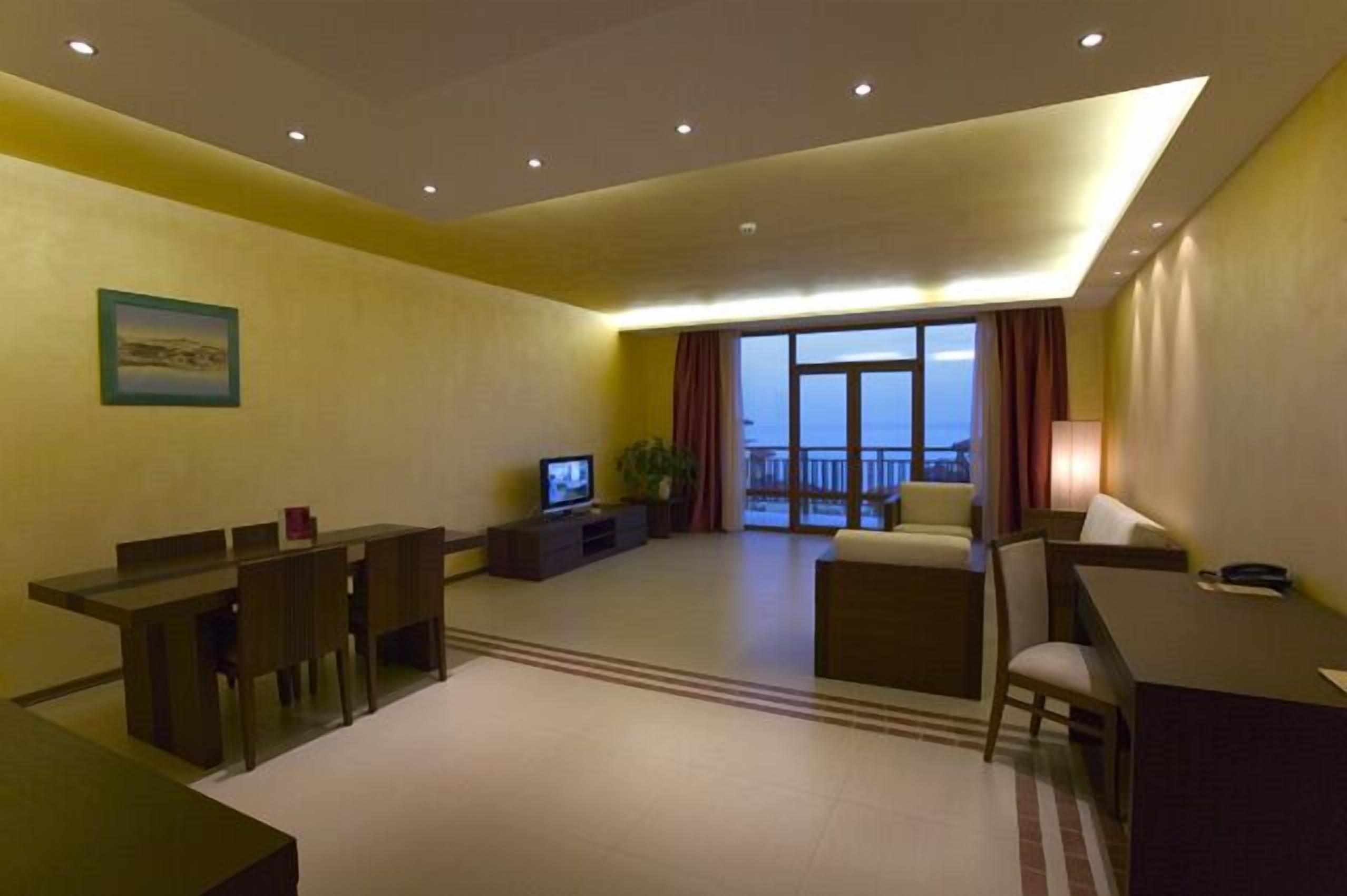 A modern hotel room with a dining area, a TV, and a balcony with a view.