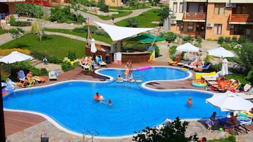 Relax by the pool surrounded by lush lawns and trees, with lounge chairs and umbrellas providing shaded areas.