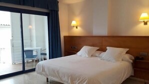 A hotel room with a bed, two bedside lamps, a small table, and a chair. - Hotel Octavia (Cadaqués)