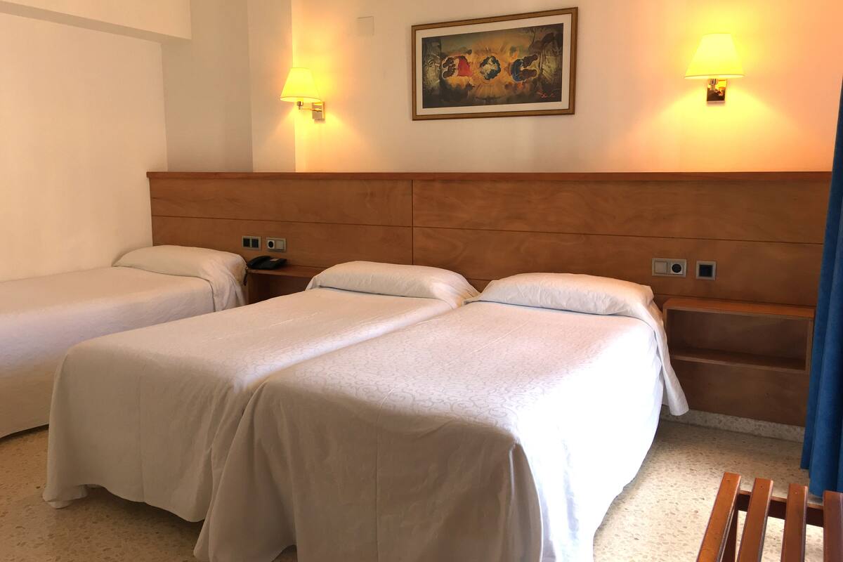 A hotel room with two single beds, a wooden headboard, bedside tables with lamps, and a painting on the wall.
