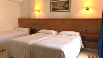 A hotel room with two single beds, a wooden headboard, bedside tables with lamps, and a painting on the wall.