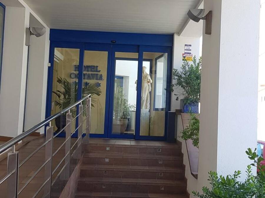 Entrada de hotel con una puerta azul, una escalera y una barandilla.