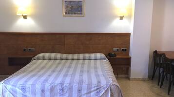 Una habitación de hotel con cama, mesitas de noche, escritorio y dos lámparas fijadas a la pared.