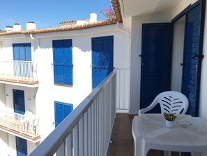 A balcony with white railing, a white plastic chair, and a small table with a potted plant.