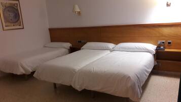 Une chambre d’hôtel avec deux lits simples et un lit plus grand, une tête de lit en bois, des tables de chevet et une lampe fixée au mur.