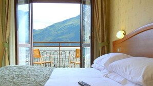 A hotel room with a bed, a remote control, and a view of mountains through a balcony. - Hotel Sole - Limone (Limone sul Garda)