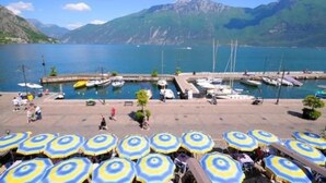 A marina with boats docked, a dock area with umbrellas, and mountains in the background. - Hotel Sole - Limone (Limone sul Garda)